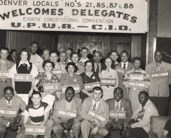 Packinghouse Educational Conference at Highlander Folk School.  Banner reads, "Denver locals No's 21, 85, 87 & 88 welcomes delegates, Eighth Constitutional Convention, U.P.W.A.-C.I.O."  Delegates are wearing tags to show their affiliation or position.