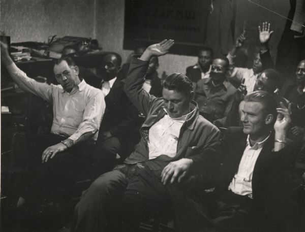 A group of smelter workers, with their hands raised as if responding to a question, at a Highlander Folk School workshop.