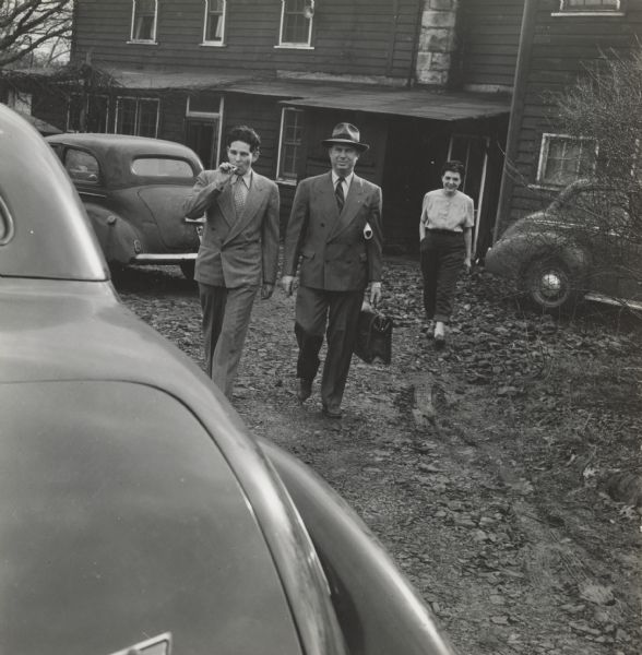 Two men walking to a car at the CIO School out in back of Highlander Folk School. Zilphia Horton walks on the right behind them.