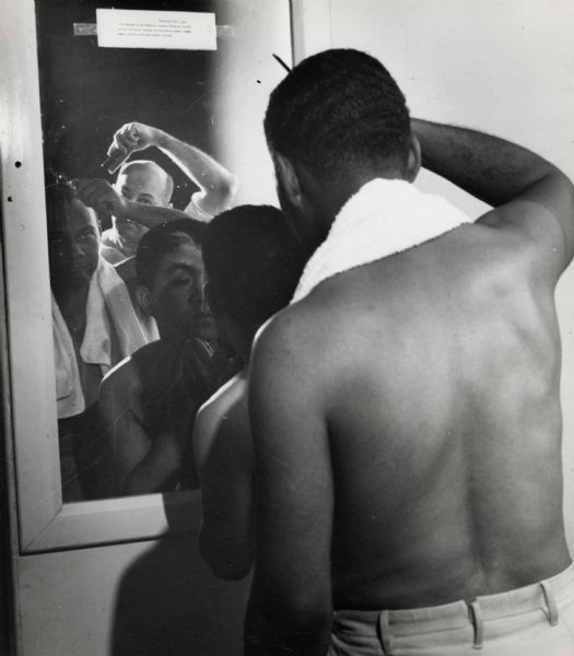 A group of men combing their hair in front of a mirror at Highlander Folk School.