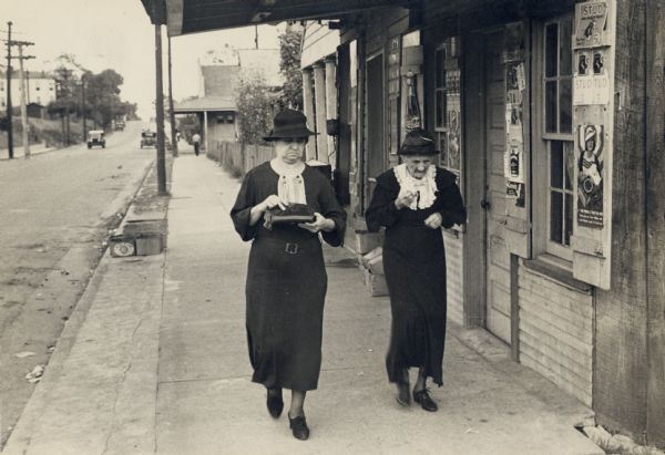 Two elderly women walking on a sidewalk next to a storefront.