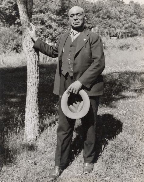 A member of the Food, Tobacco and Agriculture workshop at Highlander Folk School posing near a tree with a fedora and cigar in his hand.