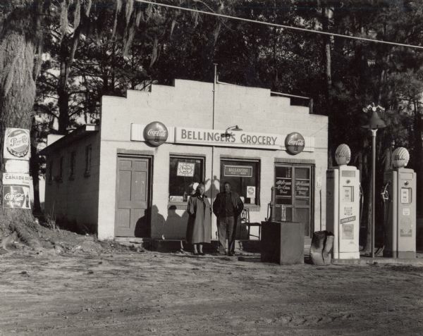 A man and woman standing in front of Bellinger's Grocery store and gas station.