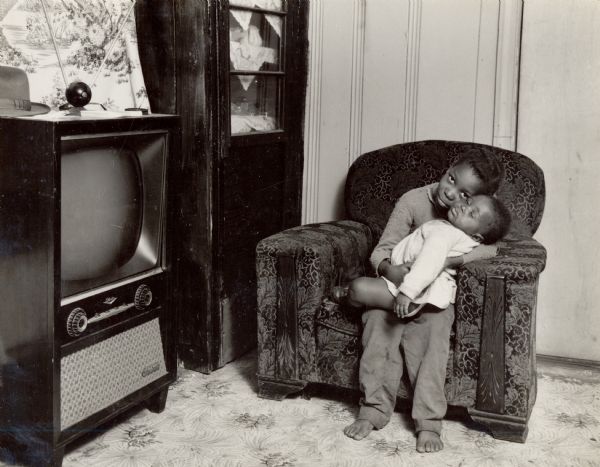 A child holding a baby next to a television on Johns Island. Part of the Citizenship group that convened there.
