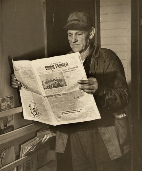 A man, presumably a farmer, reading "The Tennessee Union Farmer" newspaper.