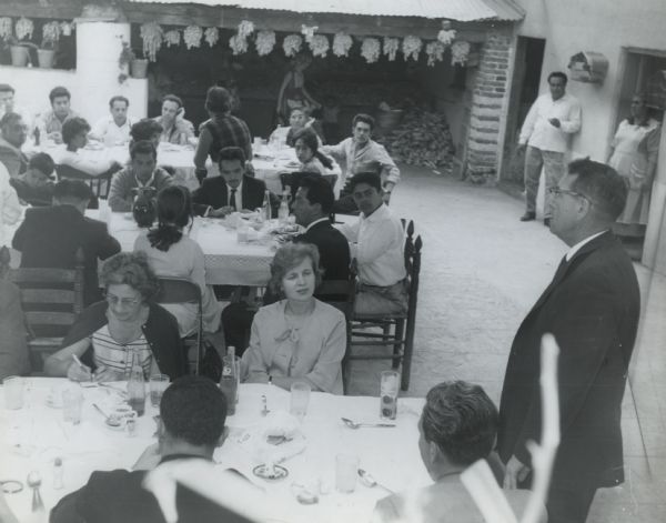 A village near Cuautla, Mexico, where the Highlander-sponsored, Inter-American Educational Adults seminar was held, invited participants to a committee meeting in the square. Myles Horton is to the right, speaking.  Inscription on back reads, "...as long as the urgent economic reforms and social injustices are not solved in Turkey--in particular, the very serious unemployment which is said to amount to something like twenty percent of the whole working population--I think that as long as these problems are not solved, the attractiveness of communism as a political method is bound to increase in Turkey. -- Interpreter: (voice over) Even in metropolitan Turkey, in the large cities you'll find them, the public letter writer.  They're the reminder that all these questions, of communism and reforms and unions, are placed for decision before a population largely illiterate.  The educated voter, schooled enough to handle even his own correspondence, is a minority in Turkey.  Public letter writes in street booths." Aimee Horton can be seen at the front table on the right.