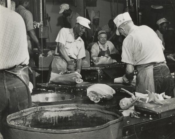 A group of packinghouse workers from an unidentified location processing pigs.