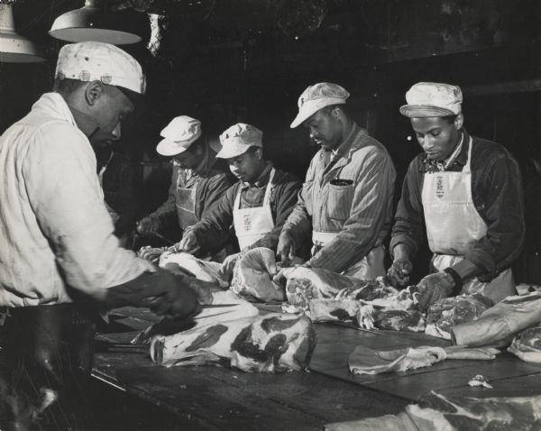 A group of African American packinghouse workers at an unidentified location cutting slabs of pork.