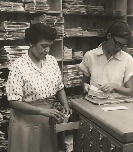 Two women searching through a card catalog, standing in front of a stack of periodicals.  Possibly inside the Highlander Folk School Library.