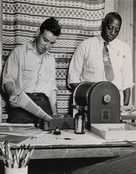 Two men creating pamphlets using a mimeograph duplicator machine at Highlander Folk School.  The African American man to the right is wearing a button that reads, "Shop Steward."