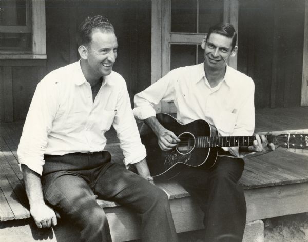 Two CIO members sitting on porch outside of the Barton recreational department cabin at Highlander Folk School. One of the men is playing a guitar.
