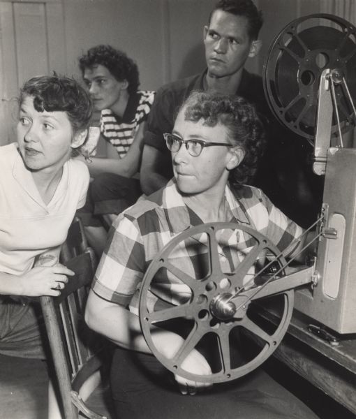 Zilphia Horton(?) learning to operate a film projector at Highlander Folk School. Three people observe behind her.
