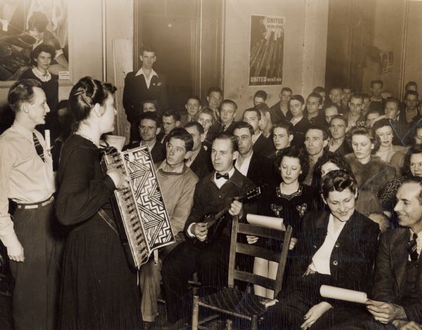 Zilphia Horton leading songs at Highlander during an early union CIO session. Charlie Wilson, board member, extreme right, next to him is his wife Frankie. Both were students at Highlander in early 1930s.  Man in front is playing a mandolin. Mary Lawrence, top left; Waldemar Hille (?), left of Zilpha.