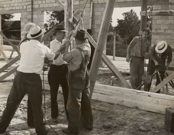 An unknown group of men lifting a pulley in the process of constructing an unknown building.  A man in the background is filming the process.
