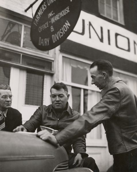 Virginia Farmers Union coop members leaning on a car.  Sign above reads, "Farmers Union... Inc. Office-Warehouse & Dairy Division".