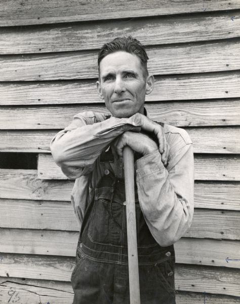 Portrait of a farmer standing outside of a wooden structure.