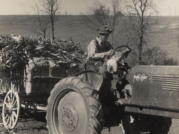 A man and a boy in an Oliver "Row Crop 60" tractor, pulling a full load.