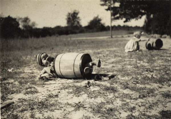 A boy named Henry rolling down a hill in an old nail keg.  Part of the Highlander Folk School nursery. There is also a girl in the background with another nail keg.