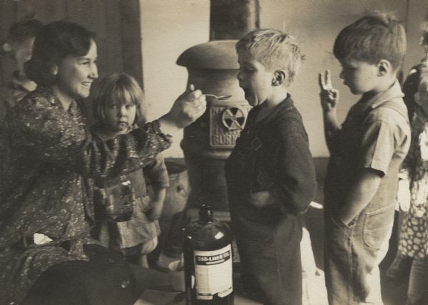 A woman giving Highlander nursery school children cod liver oil.