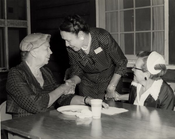 Eleanor Roosevelt, on left, shaking hands with Mrs. Jennings Perry, standing. May Justus is on the right. At Highlander Folk School. Possibly part of 25th Anniversary festivities.