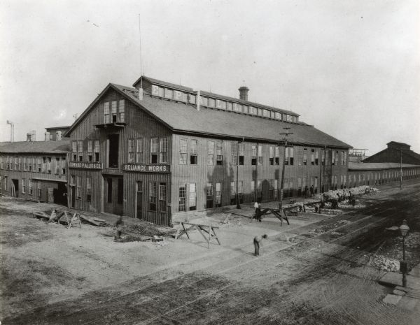 Section of the factory at a crossroads with road construction workers outside. Name of company visible on building.