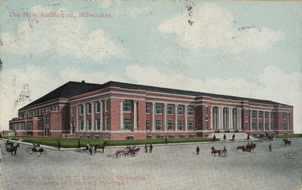 Color postcard of the New Auditorium. The road in front has three cars, several horse-drawn carriages, and several people. Caption reads: "The New Auditorium, MilwaukeeMil."