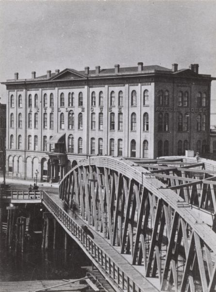 Axtell House, located at Walker's point on the corner of S. Water and Ferry Streets. There are pedestrians on the bridge over the river.