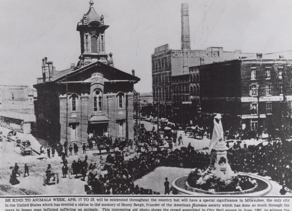 Elevated view of fountain in front of the old City Hall, with a memorial to Henry Bergh (?-1888), founder of the American Humane Society. Several other buildings are in the background, including the Chas. Baumbach Co. There is a large crowd of people as well as horses and horse-drawn vehicles.