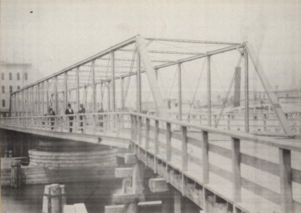 Metal bridge over river with three men standing near the railing.