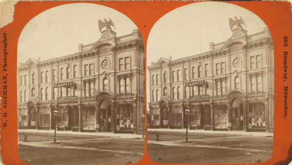 Stereograph; view of store and adjoining buildings, Wisconsin and Milwaukee Streets.  A large statue of a bird sits atop the store in the right of the image.  Store windows are visible, as well as signs for carpets.