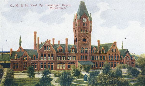 Elevated view across lawn with paths among trees toward the Passenger Depot with tall clock tower. Caption reads: "C. M. & St. Paul Ry. Passenger Depot, Milwaukee."