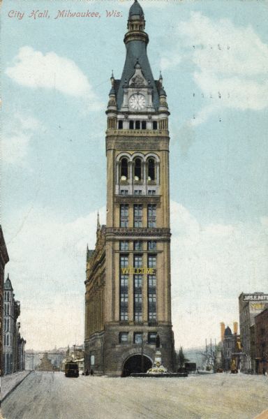 Color image of City Hall with a welcome sign on the front of the building.  The Henry Bergh monument fountain is in front, and  a trolley is on the left side of the building. Caption reads: "City Hall, Milwaukee, Wis."