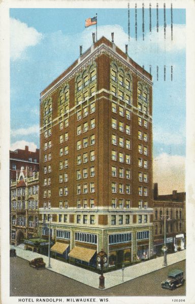 Elevated view of the Randolph Hotel with a flag flying from the roof.  A clock is on a pedestal at the street corner. Caption reads: "Hotel Randolph, Milwaukee, Wis."