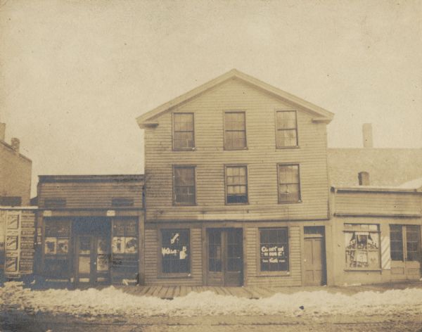 Front view of three-story building located on the south side.  Buildings on either side have storefronts, and snow is on the ground.