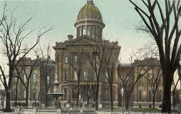 Colororized view of the front of the courthouse. Bare trees surround a fountain in the front, which has the top-most part of the dome cut-off by the frame. Caption reads: "Court House, Milwaukee, Wis."