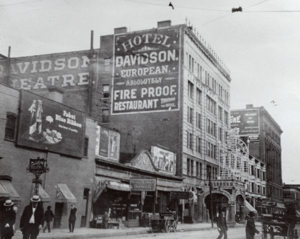 Davidson Theatre and Hotal at 135-137 Third Street. Signs for advertisements identify the buildings that are visible.  Carriages and people are on the road in front of the theater.