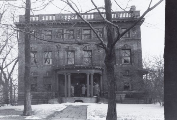 Exterior of building just prior to demolition. At the time, the building was occupied by the Milwaukee County Historical Society.  Three and one-half story square building. Entrance has small rounded porch with a brick pathway leading up to the door. A group of people are gathered on the small porch.