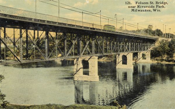 Later renamed Locust Street, the bridge spans the Milwaukee River near Riverside Park. Elevated view from shoreline. A trolley and a pedestrian are on the bridge. Supports are iron on top of brick. Caption reads: "Folsom St. Bridge, near Riverside Park, Milwaukee, Wis."