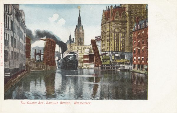 Colored view of the river lined with buildings. The drawbridge is raised as a steamboat is passing through. There is a clocktower in the background. Caption reads: "The Grand Ave. Bascule Bridge, Milwaukee."