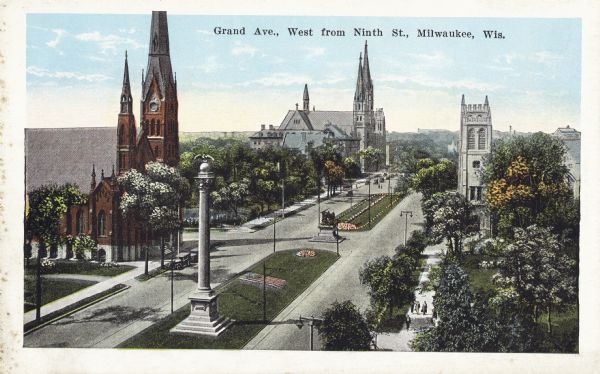 West from Ninth Street. Elevated view taken from on top of a building. Churches and trees line the road, which has a strip of land with monuments in the middle of the avenue. Caption reads: "Grand Ave., West from Ninth St., Milwaukee, Wis."