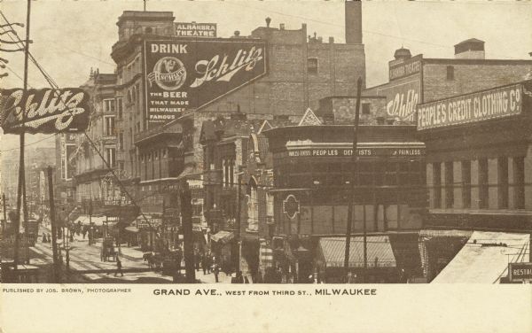 West from Third Street. Advertising signs for Schlitz, People's Credit Clothing Co., Peoples Dentist, and other businesses line the buildings along the road. Caption reads: "Grand Ave., west from Third St., Milwaukee."
