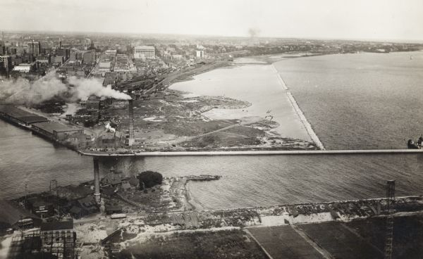 Aerial view of city, river and harbor. Two smokestacks are on either side of the river mouth.