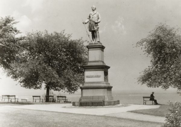 Monument in Juneau Park.  A man is sitting on a bench, with Lake Michigan behind.