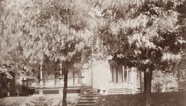 Located on 4th Street; only the first floor is visible through the trees.  The house sits on a small hill above the street.  Two chairs sit in the lawn on the right.