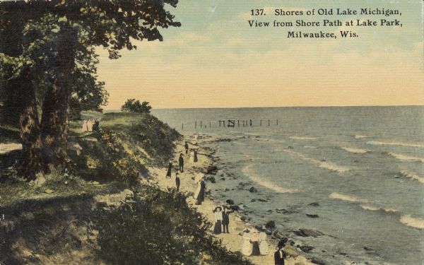 Path along Lake Michigan beach. Below are people walking along the shoreline. Further down the path is a small group of people. Pilings are in the water in the background. Caption reads: "Shores of Old Lake Michigan, View form Shore Path at Lake Park, Milwaukee, Wis."