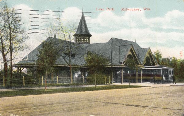 View across road toward a large pavilion with a gray roof and tower. A dirt road passes across the lower foreground. On the right of the building is a trolley and three men. Caption reads: "Lake Park , Milwaukee, Wis."