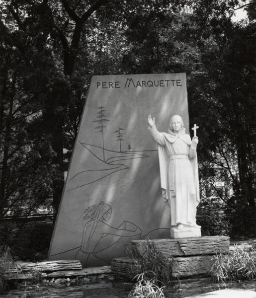 Statue of the monk with a cross in his left hand and his right hand upraised. Behind the statue is a plaque with a carving of an Indian in a canoe near a shoreline, as well as the title "Pere Marquette."Located in a park at the Chicago, Milwaukee & St. Paul Railway station.  The students of Marquette High School raised the money for the monument.