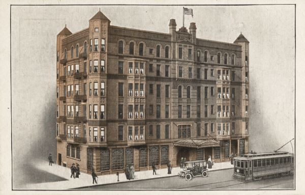 Elevated view of hotel on Wisconsin Street. The hotel was opened for business in January of 1914. A flag is flying from the roof.  Pedestrians are walking on the sidewalk in front of the building and a car is parked in front with a streetcar passing the front entrance.
