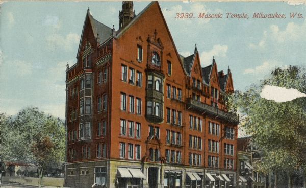 View towards the large, red building with steep roof. First level has awnings above windows. Behind the building is a grassy area. Caption reads: "Masonic Temple, Milwaukee, Wis."