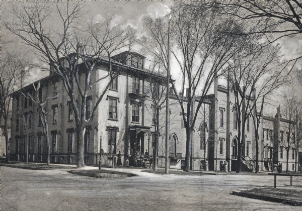 The central gothic structure was built around 1852 for the Milwaukee Female College and the wings were added at a later time.  Later this building was used as the Hotel Carlton.  It stands (in 1939) at the southeast corner of Juneau Avenue and Milwaukee Street. Women and children are standing in front of the building.